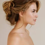 Luxury bridal updo hairstyle with soft face-framing pieces, textured low bun, dimensional brunette balayage.