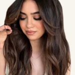 Dimensional espresso brunette hair color with soft face-framing highlights, polished waves, and reflective shine.